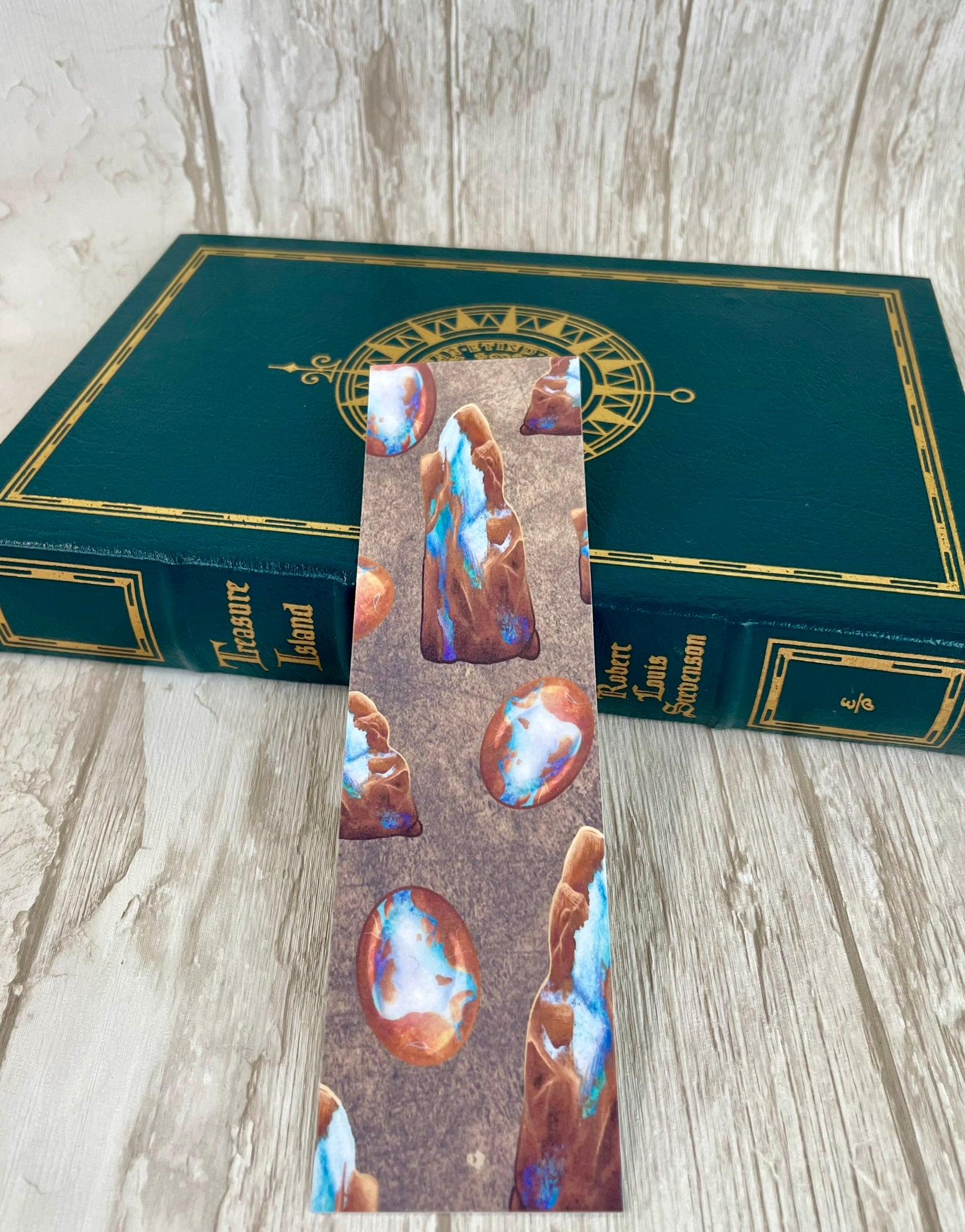 A 2 by 7 inch bookmark featuring various raw and cut boulder opals against a background that looks like a rough cut rock texture