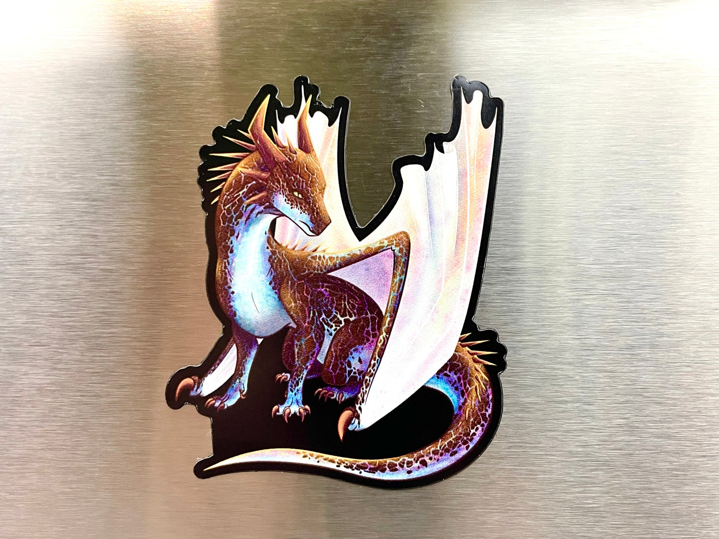 A flat magnet featuring a side sitting dragon that has boulder opal features with iridescent wings