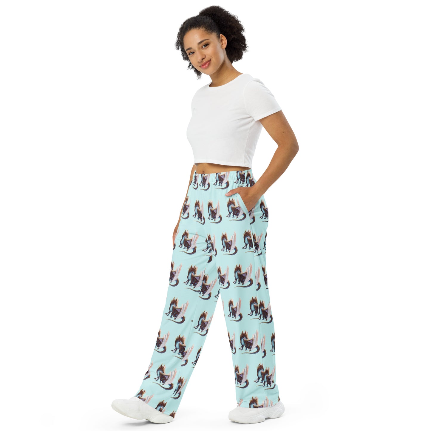 Side view of unisex, light bluish green in color all over print pajama pants featuring a sitting, side profile of a dragon that has the features of a boulder opal with hues of blue, green, purple, and pink on the underbelly and cracks of the rough, brown hue, rock scales. The wings are tucked back and are of an iridescent shimmery hue