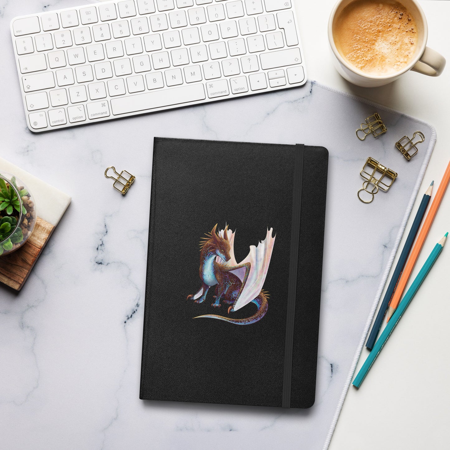 A black notebook with an elastic closure, 80 lined pages, a ribbon bookmark, and pocket in the back with the front featuring a sitting, side profile of a dragon that has the features of a boulder opal with hues of blue, green, purple, and pink on the underbelly and cracks of the rough, brown hue, rock scales. The wings are tucked back and are of an iridescent shimmery hue