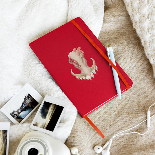 A 80 page, red hardback lined journal with a pocket in the back, a ribbon book mark, and elastic closure,  featuring a front facing warthog skull with 3 different kinds of fungi growing out of it