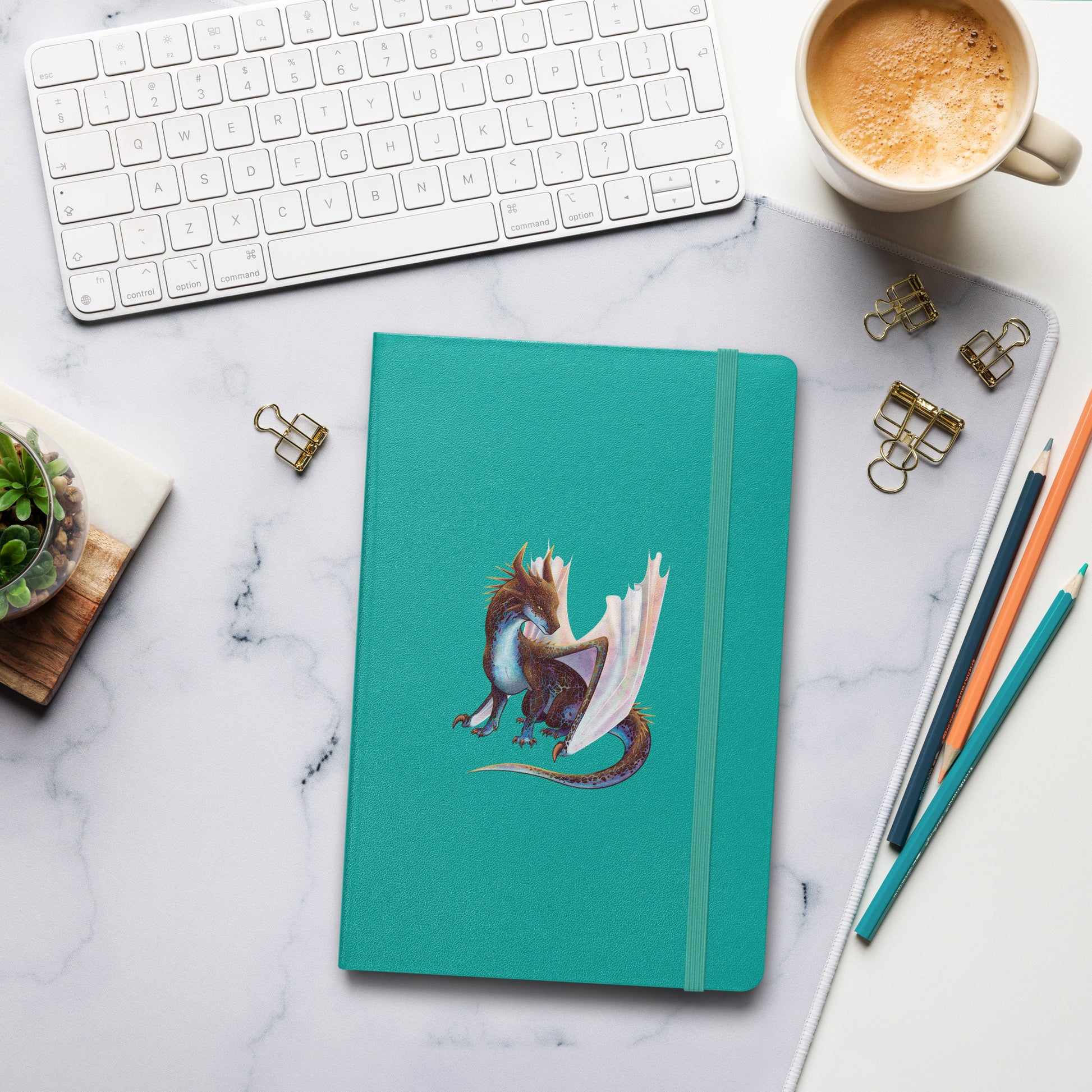 A turquoise notebook with an elastic closure, 80 lined pages, a ribbon bookmark, and pocket in the back with the front featuring a sitting, side profile of a dragon that has the features of a boulder opal with hues of blue, green, purple, and pink on the underbelly and cracks of the rough, brown hue, rock scales. The wings are tucked back and are of an iridescent shimmery hue