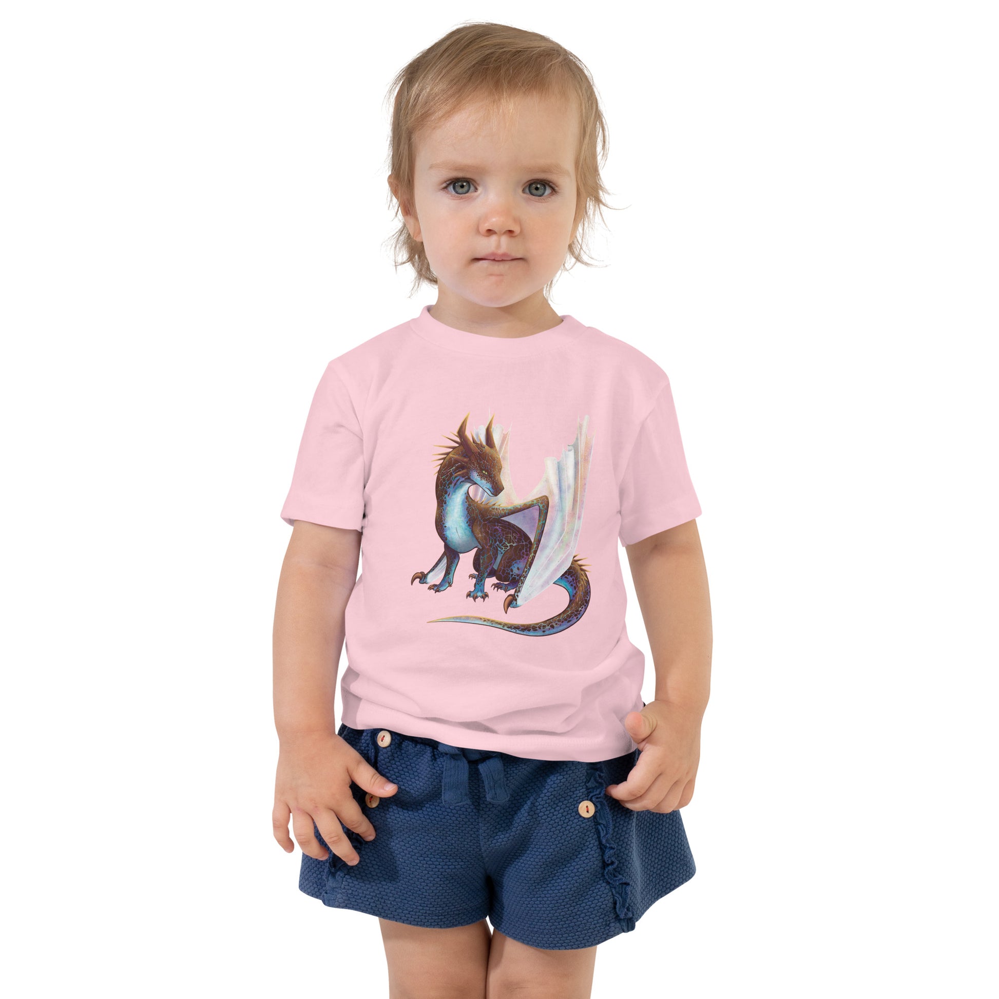 Unisex, light pink in color toddler tee shirt featuring a sitting, side profile of a dragon that has the features of a boulder opal with hues of blue, green, purple, and pink on the underbelly and cracks of the rough, brown hue, rock scales. The wings are tucked back and are of an iridescent shimmery hue