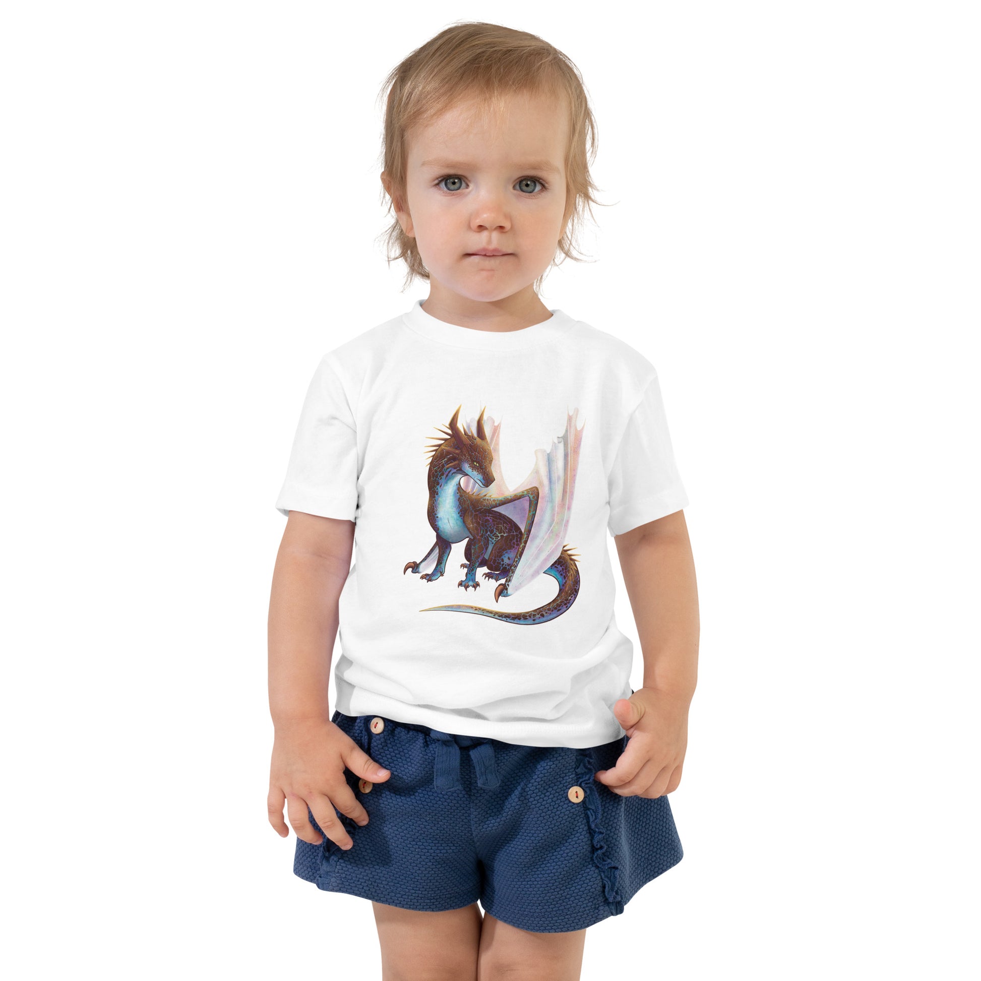 Unisex, white in color toddler tee shirt featuring a sitting, side profile of a dragon that has the features of a boulder opal with hues of blue, green, purple, and pink on the underbelly and cracks of the rough, brown hue, rock scales. The wings are tucked back and are of an iridescent shimmery hue