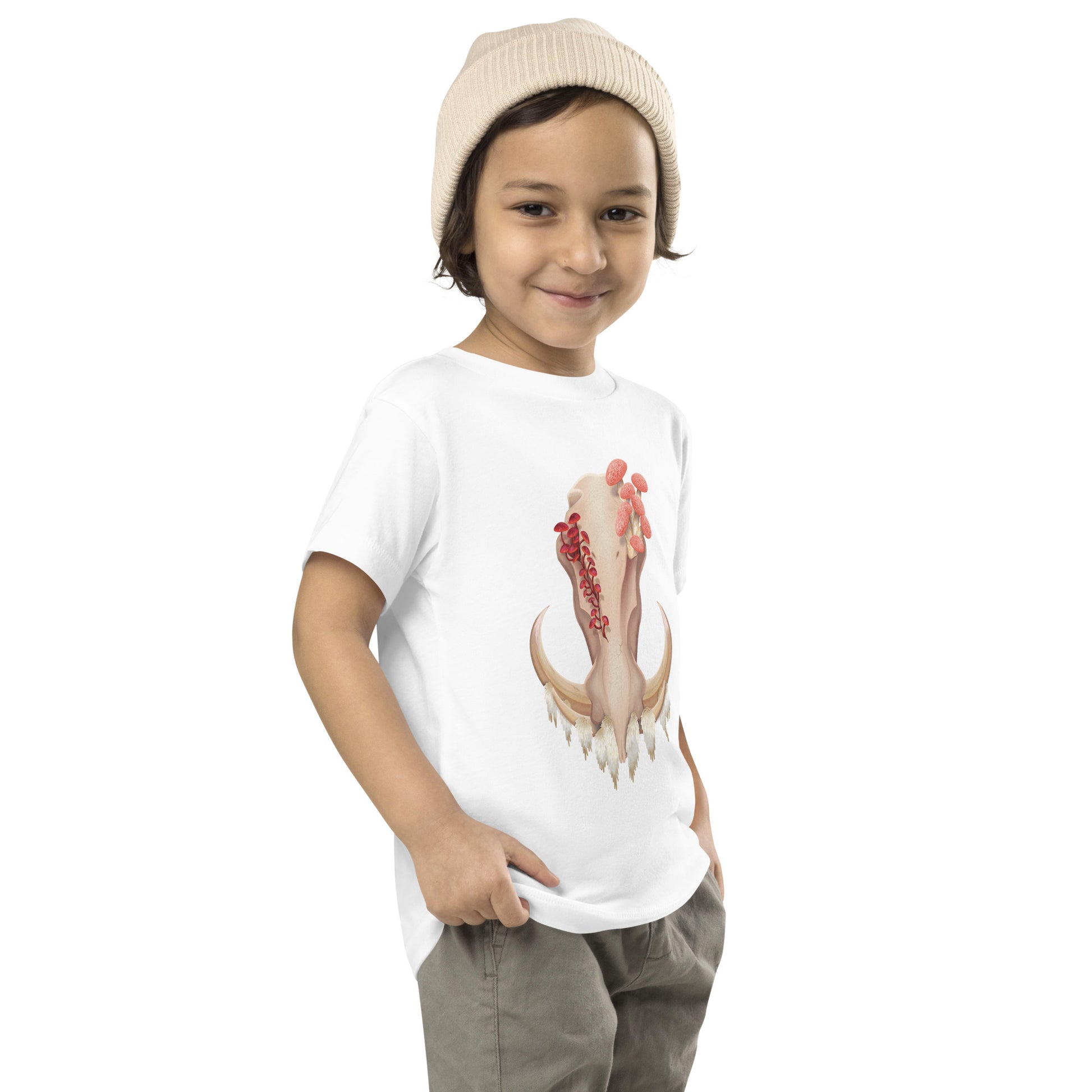 A toddler wearing a white T shirt featuring a front facing warthog skull with 3 different kinds of fungi growing out of it