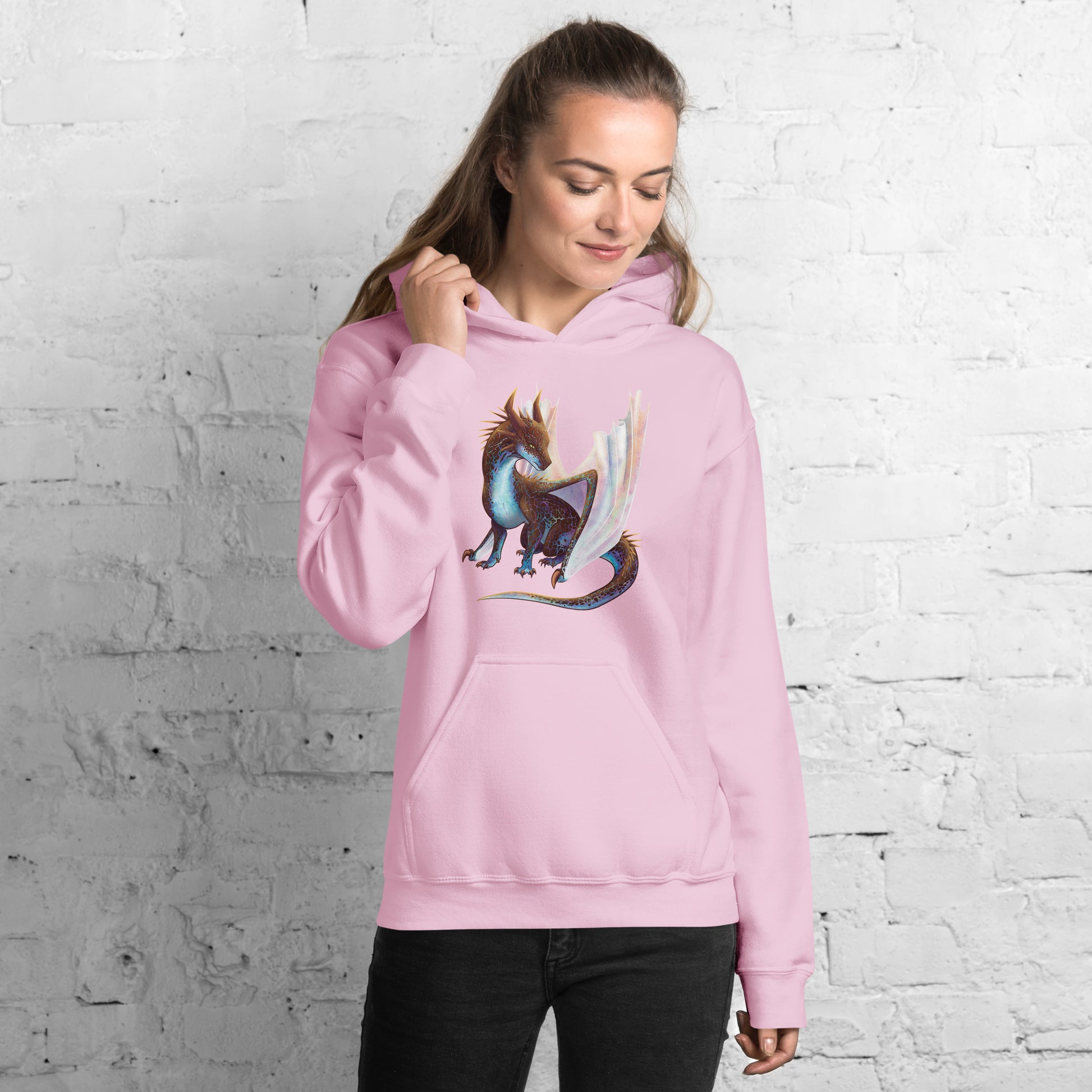 Unisex, light pink in color adult hoodie with a pocket in front featuring a sitting, side profile of a dragon that has the features of a boulder opal with hues of blue, green, purple, and pink on the underbelly and cracks of the rough, brown hue, rock scales. The wings are tucked back and are of an iridescent shimmery hue